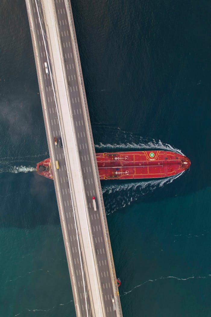 Drone shot of a red cargo ship passing under a bridge in Turkey's waterways.